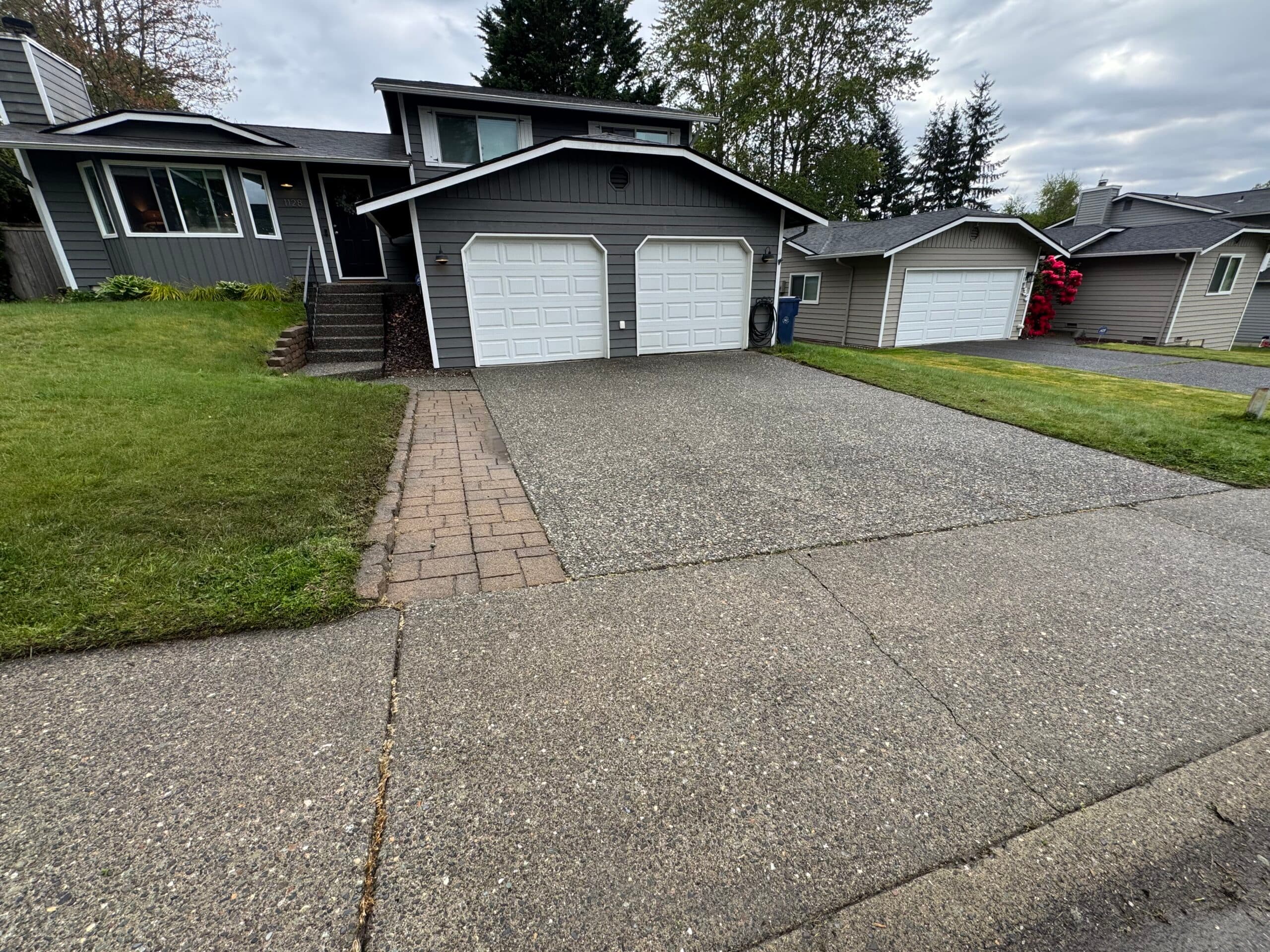 Clean exposed-aggregate driveway in front of a gray two-story home with white garage doors