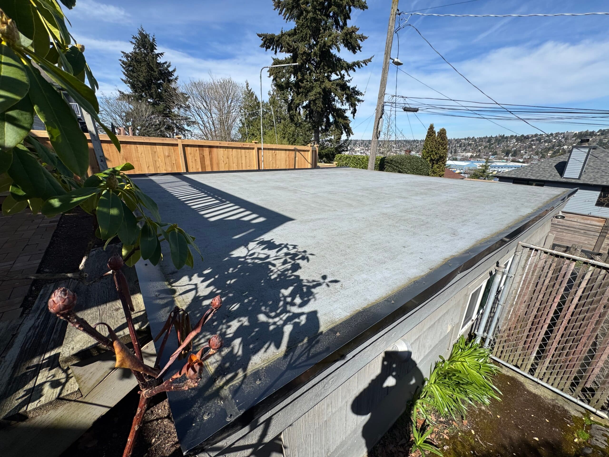 Clean flat garage roof under blue sky with a hillside behind
